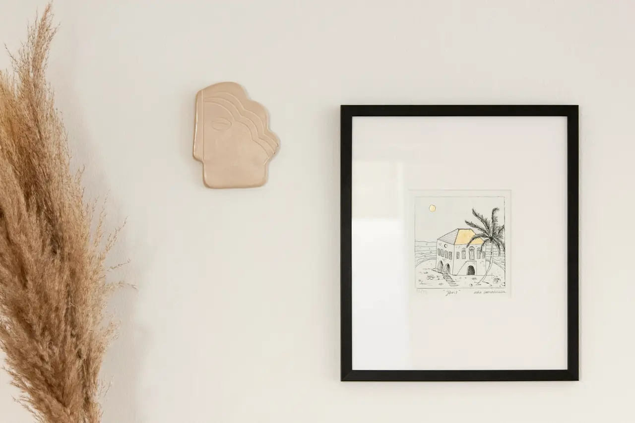 A framed print hanging on a light wall beside dried grass
